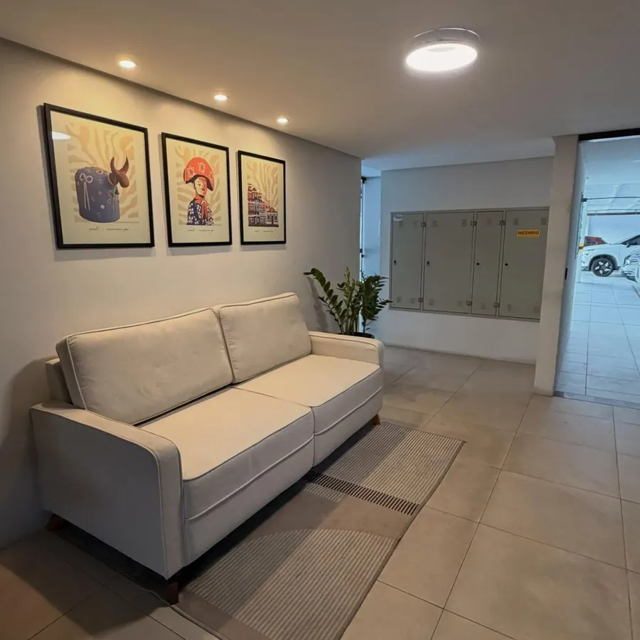Hall de entrada com sofá claro, quadros de arte regional e acesso à garagem